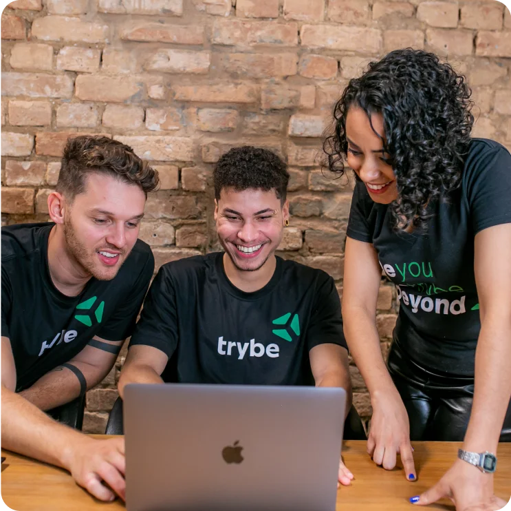 Três pessoas da Trybe em frente a um notebook